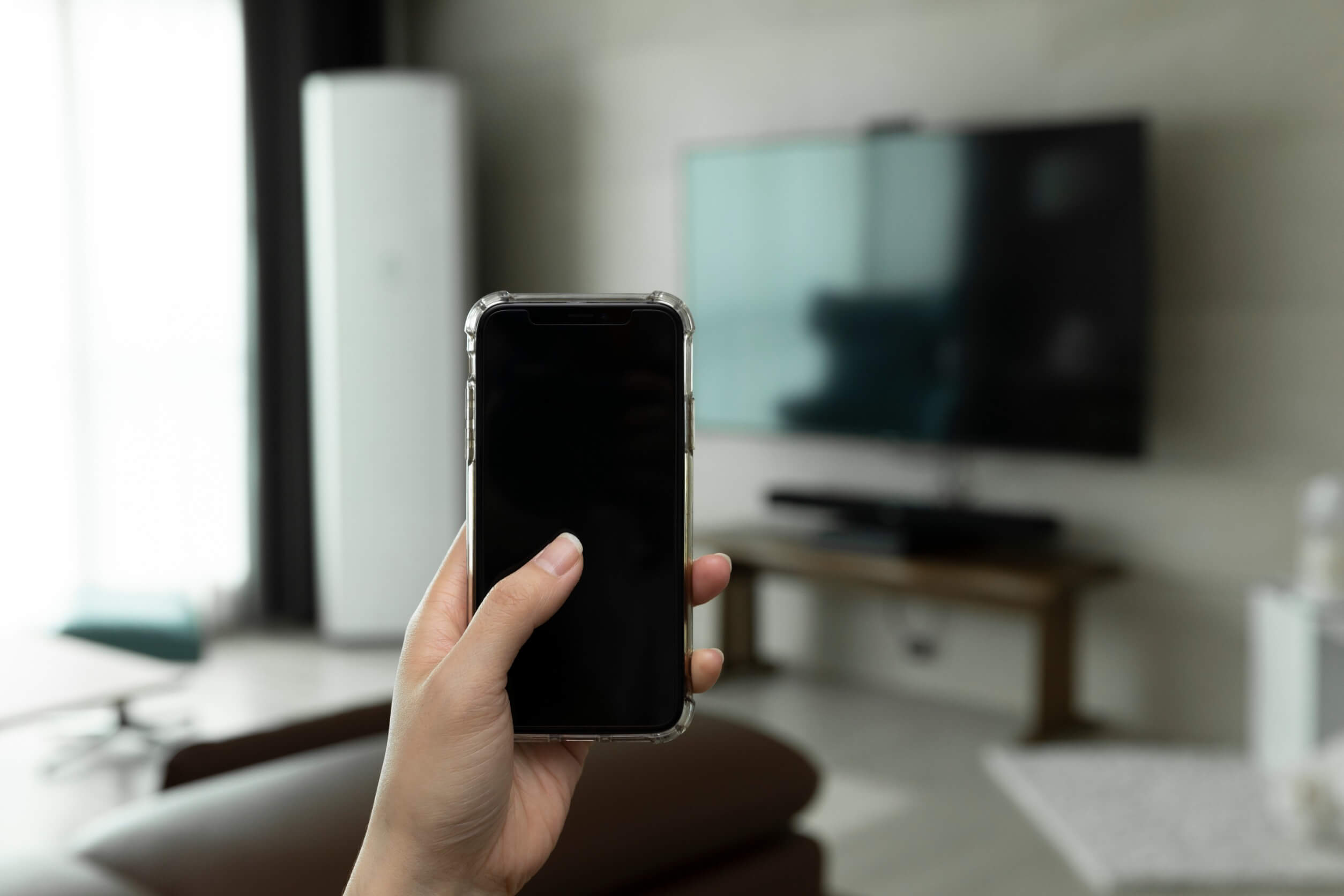 smartphone in mano con davanti una tv
